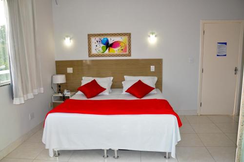 a bedroom with a large white bed with red pillows at Gran Norte Hotel - Salinas - MG in Salinas