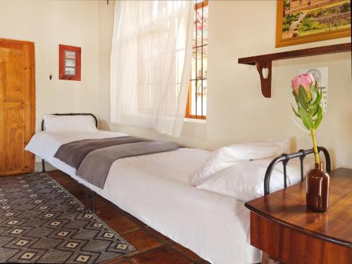two beds in a room with a table and a vase of flowers at Plaas Wegbreek in Barrydale