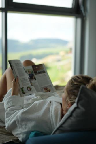 a young girl laying on a couch reading a book at Seensucht Klopeinersee in Völkermarkt