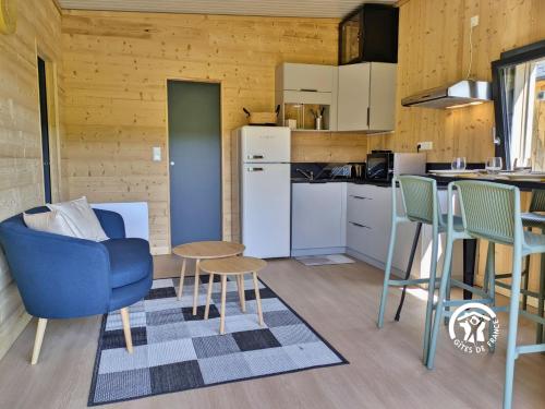 a living room with a blue chair and a kitchen at Chalet 26 Le Berthevin, Camping de Coupeau, 4 personnes in Saint-Berthevin