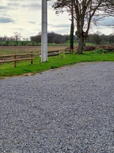 a gravel road next to a wooden fence and a tree at Un air de campagne in Saint-Pierre-la-Cour