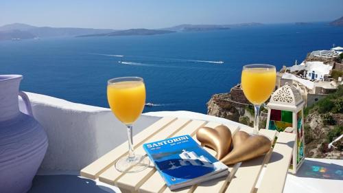 a table with two glasses of orange juice and a book at Aqua & Terra Traditional Cave Houses in Oia