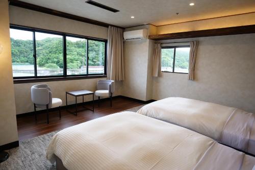 a bedroom with a bed and two chairs and windows at TAOYA Nachikatsuura in Nachikatsuura