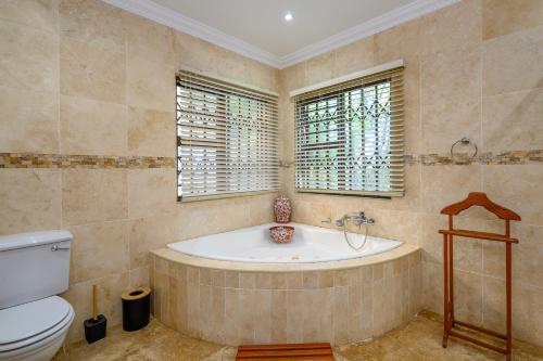 baño con bañera, aseo y ventanas en Eagle Road Holiday Home, en Umtentweni