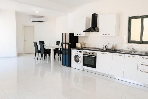 a kitchen with white appliances and a table with chairs at GuestHost - Penthouse with Jacuzzi in Gozo Island! in Marsalforn