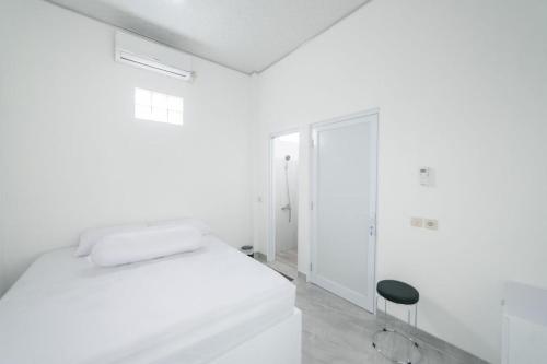 a white bedroom with a bed and a stool at DJ HOUSE Yogyakarta in Piyungan