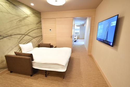 a room with a bed and a tv on a wall at Odysis Suites Osaka Airport Hotel in Izumi-Sano