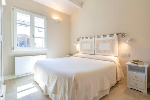 a white bedroom with a large bed and a window at Dimora Sella - Villa Ginevra in Alghero