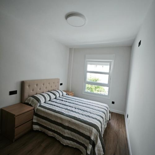 a bedroom with a bed with a striped blanket and a window at Manisa I in Ribadeo