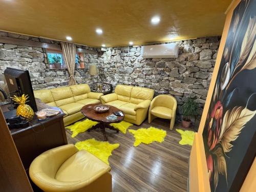 a living room with yellow furniture and a stone wall at Къща за гости Дени in Chukovezer