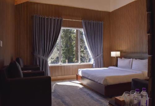 a bedroom with a bed and a large window at Roomy Mountain Top Resort, Batakundi in Battakundi