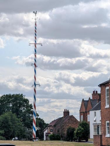 a flag pole in the middle of a field with houses at The Maypole at Wellow in Ollerton