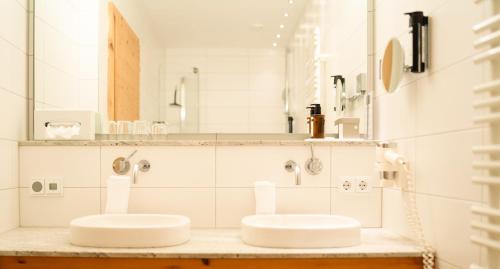 two sinks in a bathroom with white tiles at Hotel Glemmtalerhof in Saalbach Hinterglemm