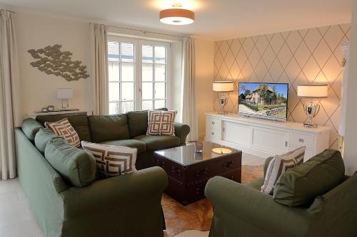 - un salon avec des canapés verts et une télévision dans l'établissement Haus Windrose, à Wrixum