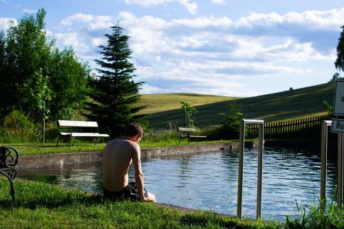 a man sitting in the grass next to a body of water at Ferienhaus Koglegg in Wies