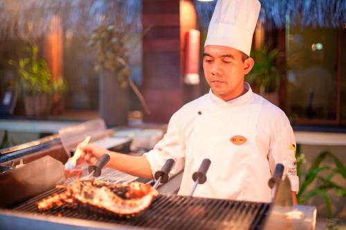 a man cooking food on a grill with tongs at Constance Halaveli in Hangnaameedhoo