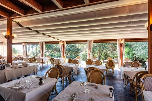 a restaurant with white tables and chairs and large windows at Roccamare Resort - Ville e Appartamenti in Castiglione della Pescaia