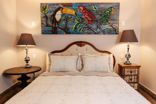 a bedroom with a bed with two lamps and a painting on the wall at Pousada Do Largo in Tiradentes
