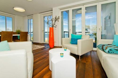 ein Wohnzimmer mit weißen Möbeln und einer orangefarbenen Vase in der Unterkunft Strandresidenzen Bansin, Ostseepalais 08 in Bansin