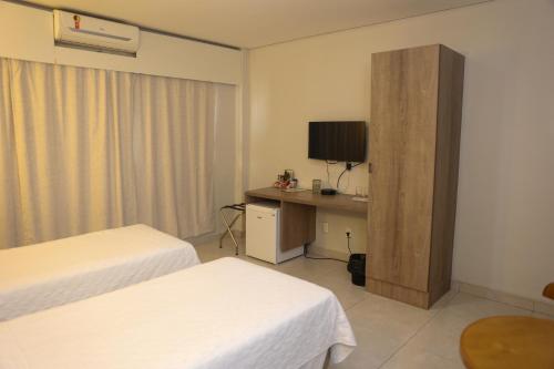 a hotel room with two beds and a desk with a television at Alfa Hotel Teresina in Teresina