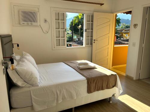 a bedroom with a white bed and a window at Sol & Aconchego Paraty in Paraty
