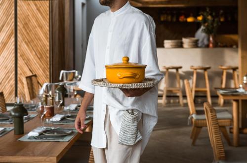 a man holding a pot on a tray in a kitchen at Phāea Cretan Malia, a Member of Design Hotels in Malia