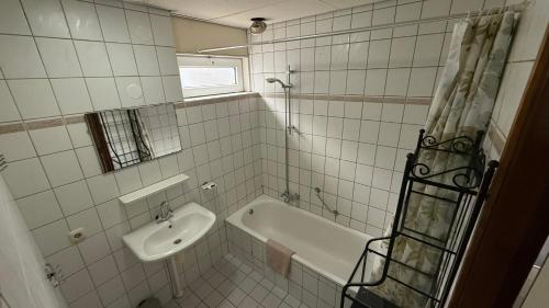 a white tiled bathroom with a sink and a bath tub at Bungalow Noordzee B in Julianadorp