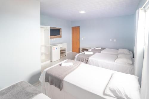 a white room with two beds and a tv at Pousada Gonçalves in Tangará