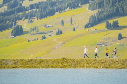 a group of people walking on a hill next to a lake at Hotel Glemmtalerhof in Saalbach Hinterglemm