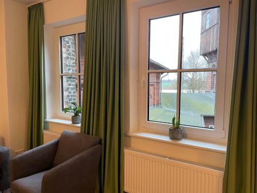 a room with two windows with green curtains and a chair at Lokschuppen Pasewalk- Gästehaus Lokschuppen in Pasewalk