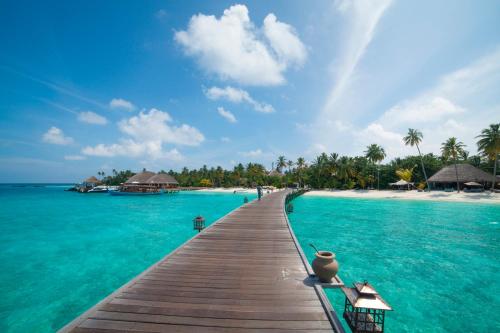 a wooden pathway leading to a beach with turquoise water at Constance Halaveli in Hangnaameedhoo