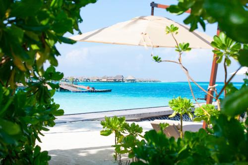 a beach with an umbrella and the ocean at Constance Halaveli in Hangnaameedhoo
