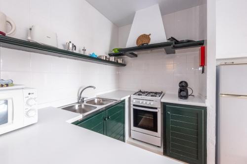 a white kitchen with green cabinets and a sink at Can Digus in Fornells