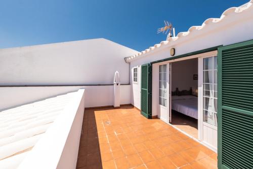 a balcony of a house with green doors and a bed at Can Digus in Fornells