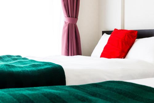 a bedroom with two beds with green and red pillows at Riverside Inn Hakata in Fukuoka