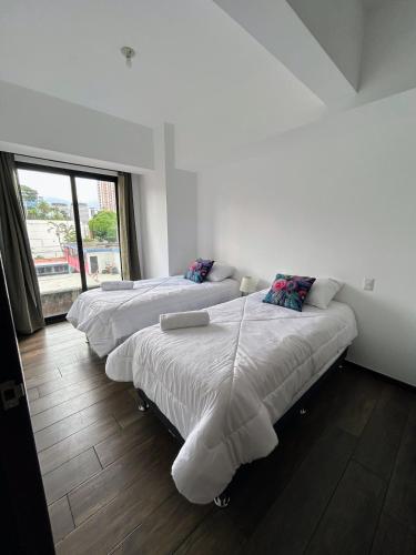 two beds in a white room with a window at Apartamento con Piscina de 2 habitaciones Edificio Brunelo Ciudad de Guatemala, Céntrico in Estación Pamplona