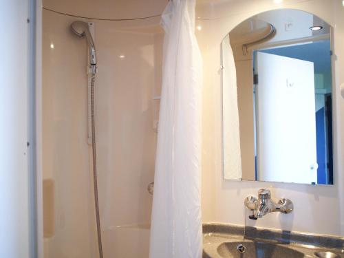 La salle de bains est pourvue d'une douche, d'un lavabo et d'un miroir. dans l'établissement Premiere Classe Niort Est - Chauray, à Niort