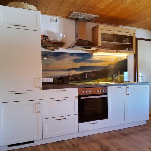 a kitchen with white cabinets and a painting on the wall at Hof Rossruck in Fischbachau
