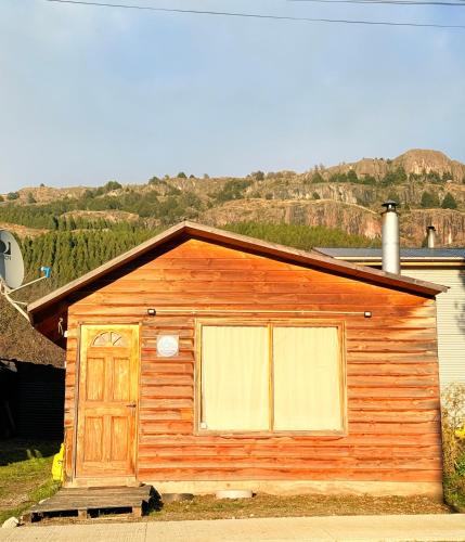 a small wooden house with a door and a hill at Casa Samtours in Puerto Tranquilo