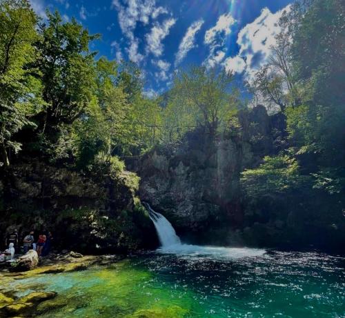 a waterfall in a river with people standing next to it at Bujtina Pllumi Theth in Theth