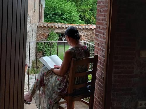 a woman sitting on a chair reading a book at Mas Vilar, relax, nature and slow Exclusive Only 6 rooms in Arbúcies