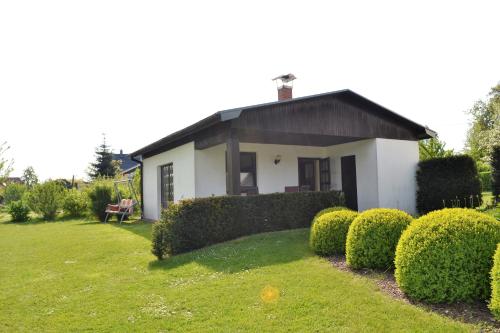 滨湖克拉科Ferienhaus am See auf großem Grundstück, Kaminofen的白色的房子,有黑色的屋顶和灌木丛