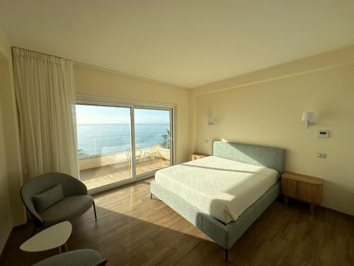 a bedroom with a bed and a chair and a large window at Blue Wave Apartment in Letojanni