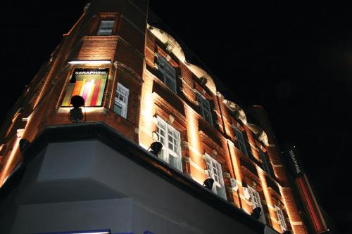 a tall brick building with a lit up tower at night at Seraphine Kensington Olympia in London