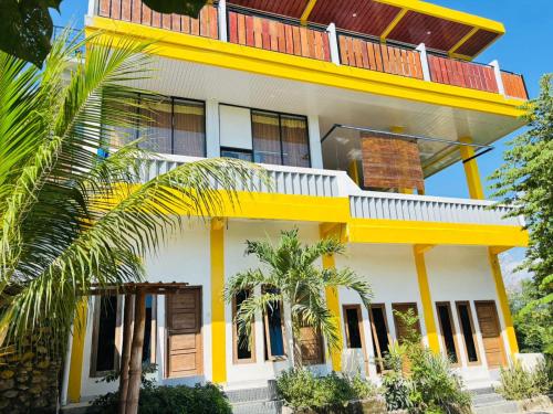 a yellow and white house with palm trees in front of it at Tarsan Homestay in Labuan Bajo