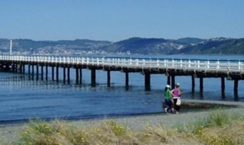 two people standing on the beach near a pier at 83 By The Sea Motor Lodge in Lower Hutt