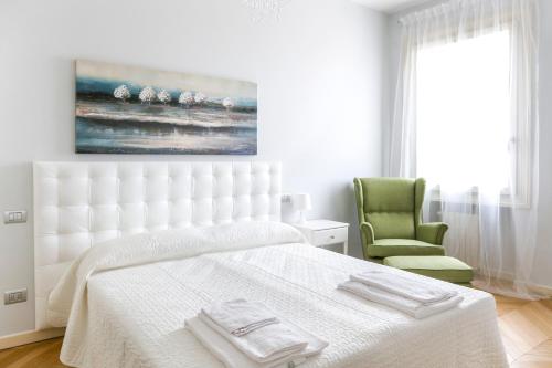 a white bedroom with a bed and a green chair at Riverside Apartment in Treviso
