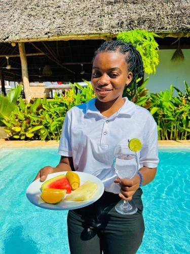 a woman holding a plate of fruit and a glass of wine at Lala salama Kendwa villas in Kendwa