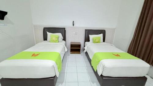 two beds in a room with green sheets at Hotel Huswah Airport in Jakarta