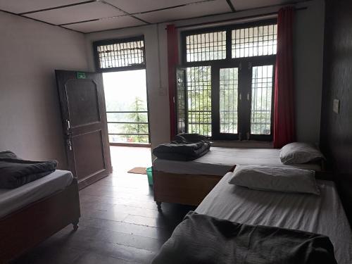 a room with three beds in a room with windows at Thrillomania Mcleodganj in Dharamshala